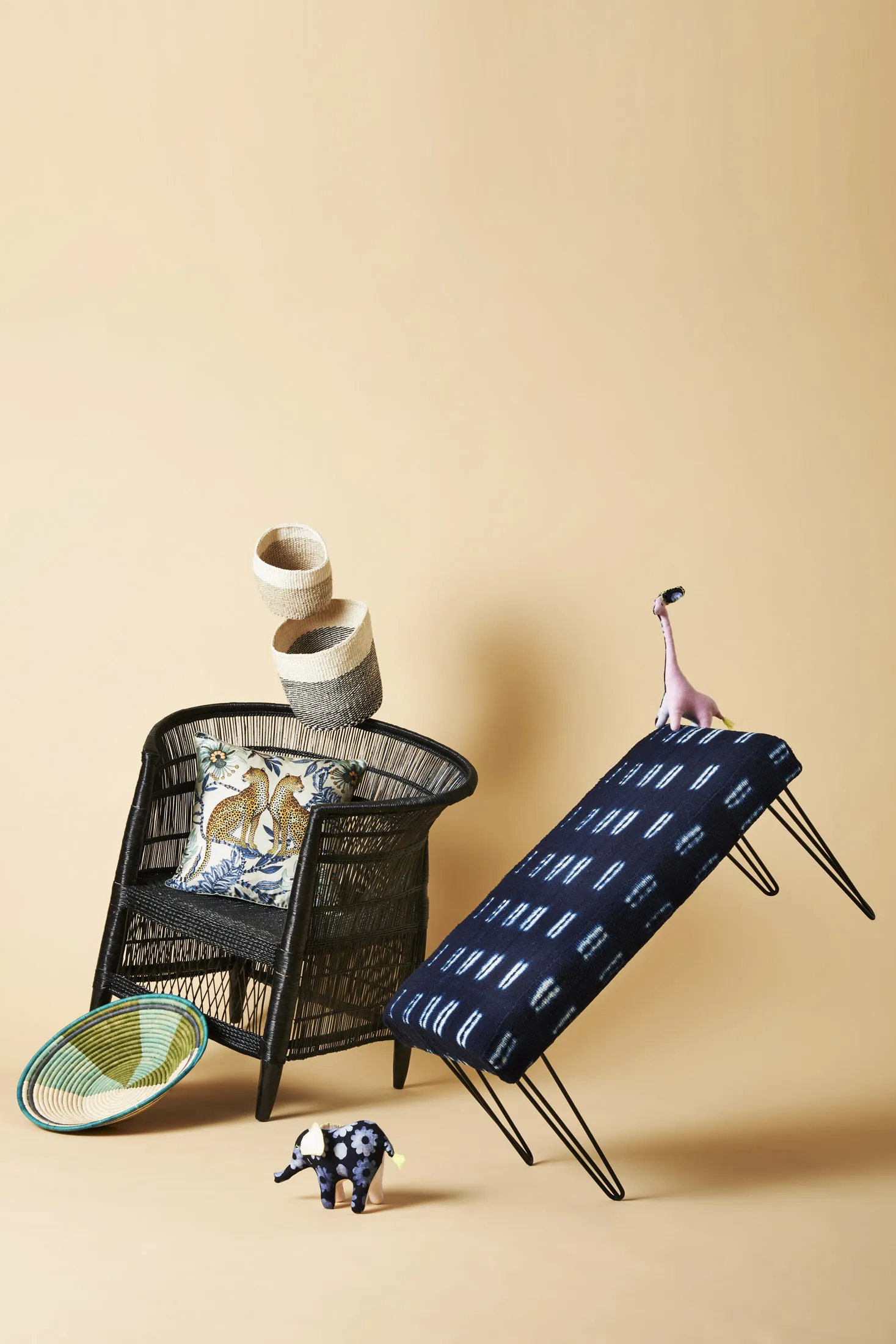 Clockwise from top: Sisal baskets ($80 for a set of three) from Katel Home. A stuffed giraffe ($30) from Indego Africa. Indigo bench ($450) available at XNasozi. Stuffed elephant ($30 from Indego Africa). A raffia bowl ($80) from Kazi Goods. A Malawi chair ($660) made of woven rattan from Ngala Trading. A Lovebird Leopards pillow cover ($175) from Ngala Trading.