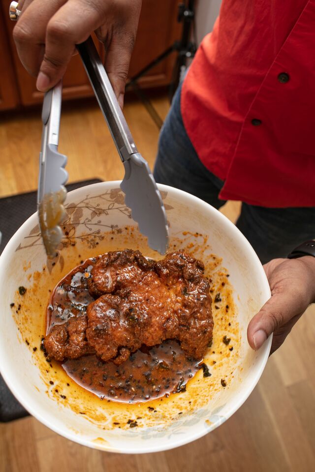 Meat in mixing bowl with oil and spices being mixed.