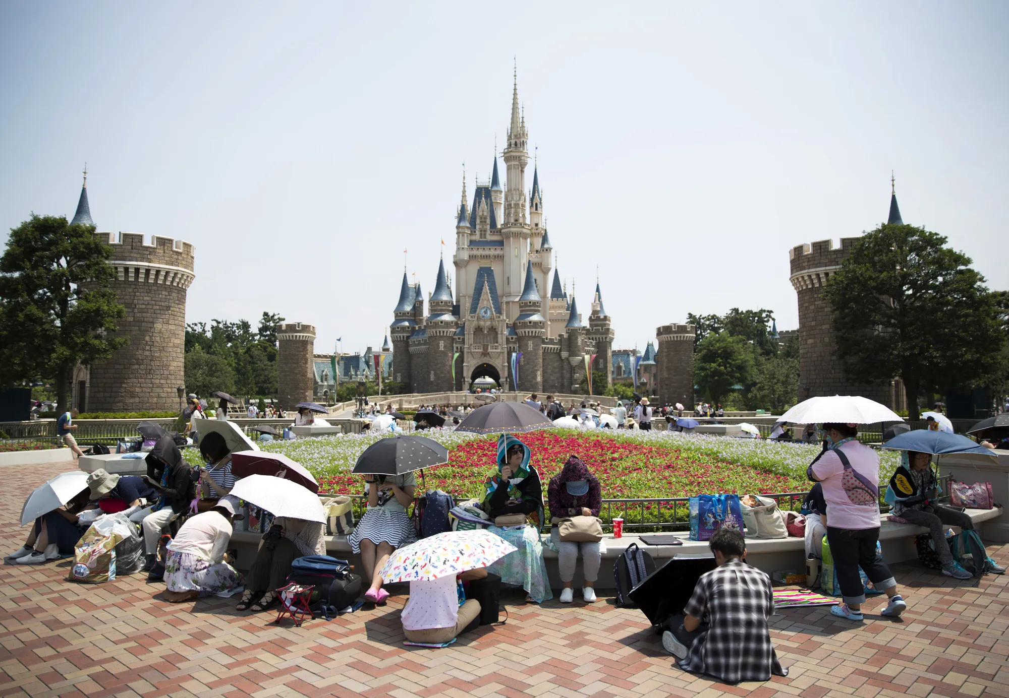 Visitors sit under umbrellas in front of the Cinderella Castle at Tokyo Disneyland.