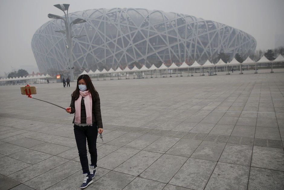A woman wearing a mask protecting from extreme smog takes a selfie in front of the Bird's Nest in Beijing.