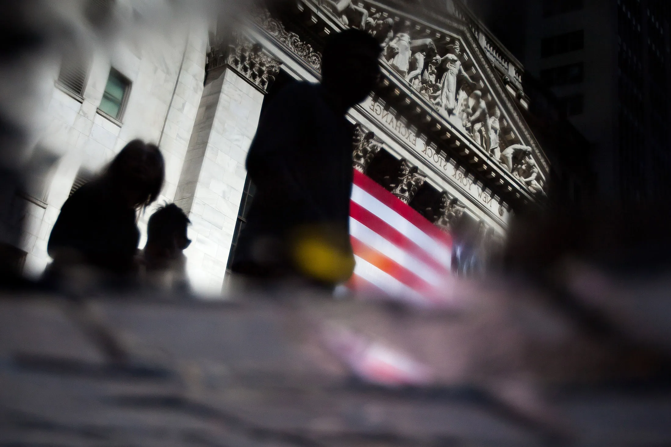 The silhouettes of pedestrians are seen in a puddle in front of the New York Stock Exchange.
