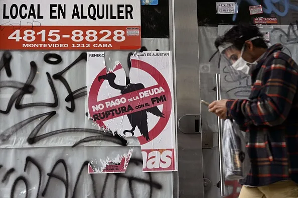 A man walks past a sign against paying the debt with the IMF pasted on a store for rent in Buenos Aires..
