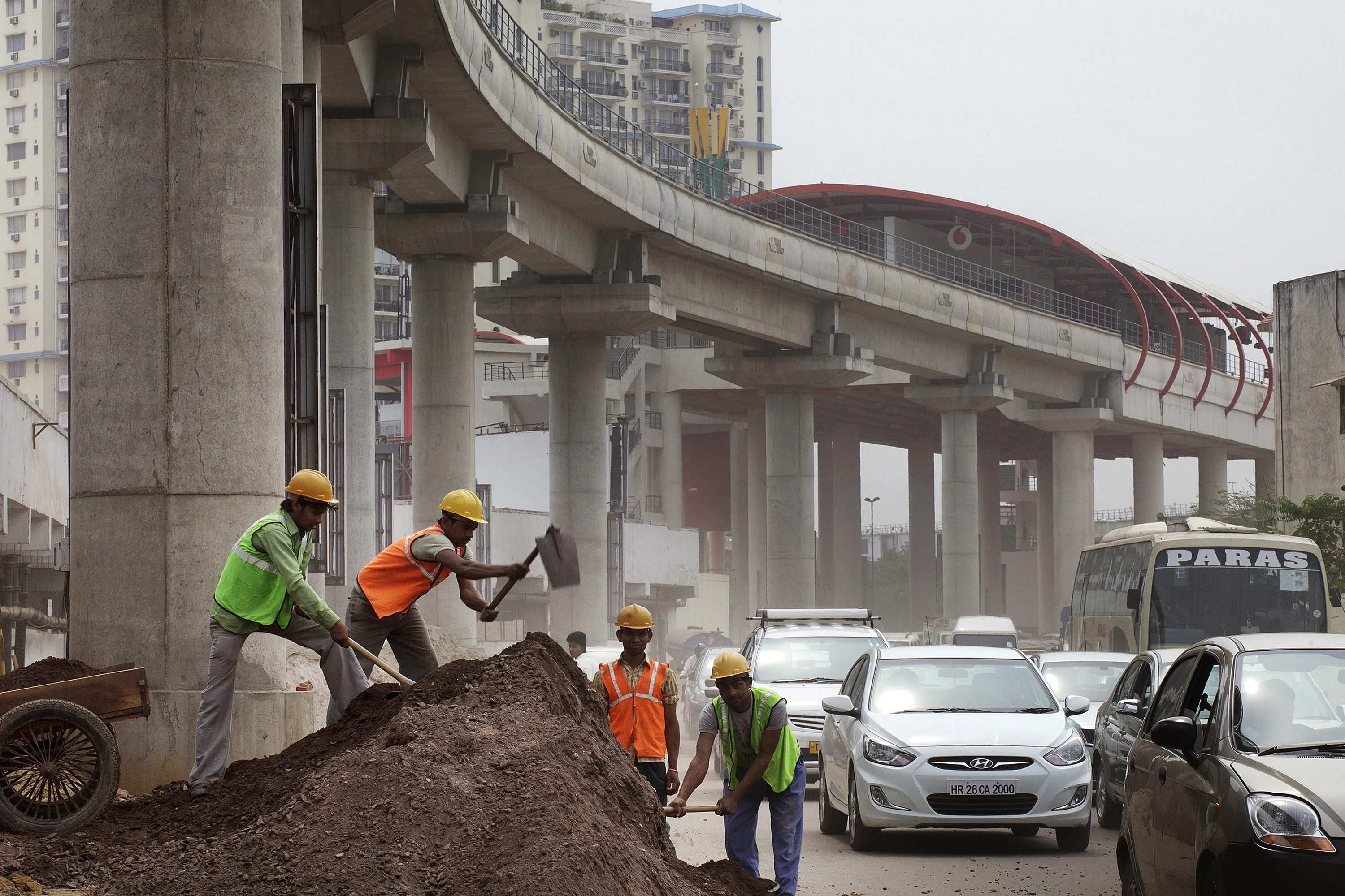 Workers labor at the roadside below an elevated track near DLF Cybercity in Gurgaon, India.
