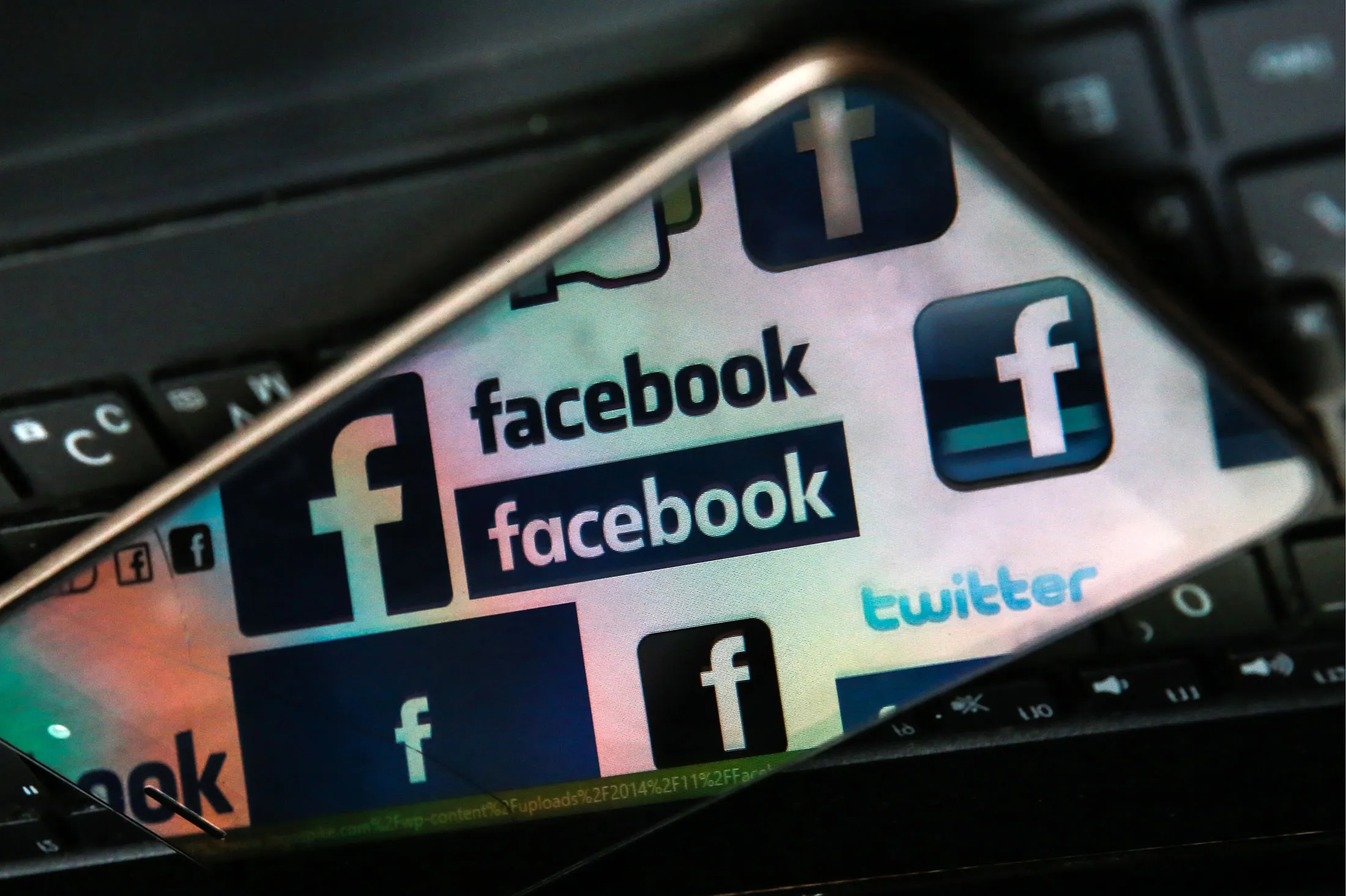 Facebook logos reflected in a smartphone screen on a computer keyboard.
