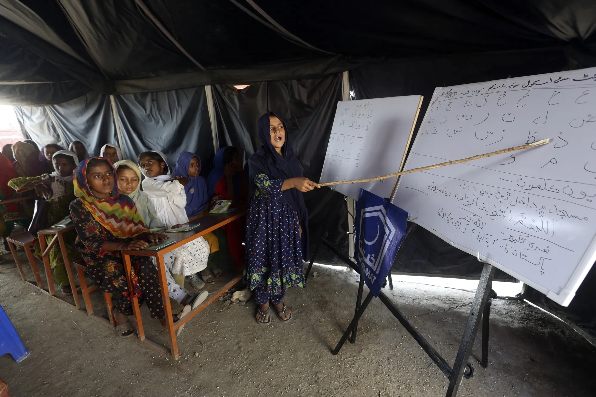 Flood affected children attend school organized by Islamic group Jamaat-e-Islami Pakistan, in Sukkur, Pakistan, Sunday, Sept. 4, 2022. Officials warned Sunday that more flooding was expected as Lake Manchar in southern Pakistan swelled from monsoon rains that began in mid-June and have killed nearly 1,300 people. (AP Photo/Fareed Khan)