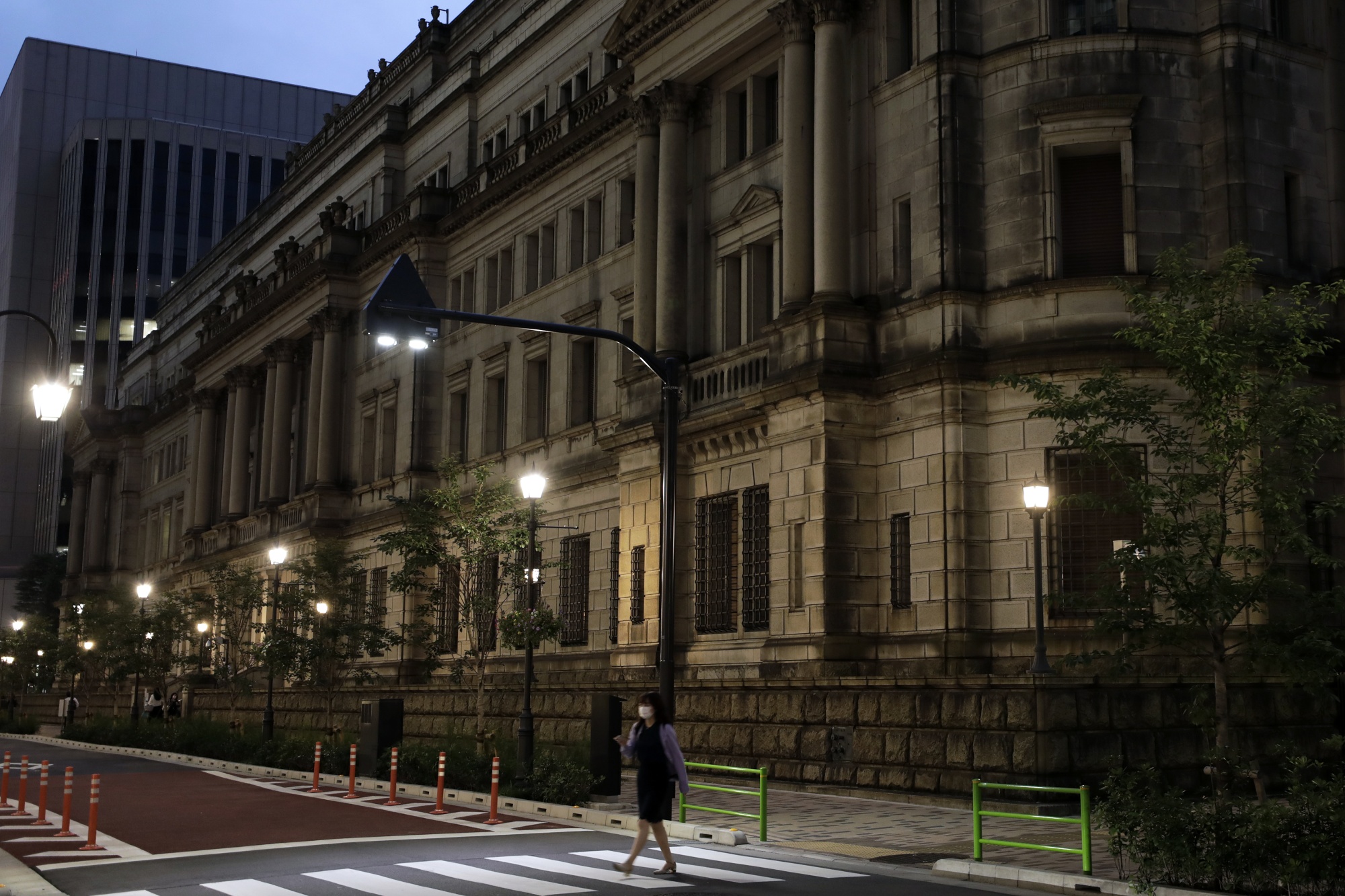 A pedestrian wearing a protective mask crosses a street in front of the Bank of Japan (BOJ) headquarters at dusk in Tokyo, Japan, on Monday, September 14, 2020. The Bank of Japan left the amount of the bond purchase unchanged at a regular operation on Monday.