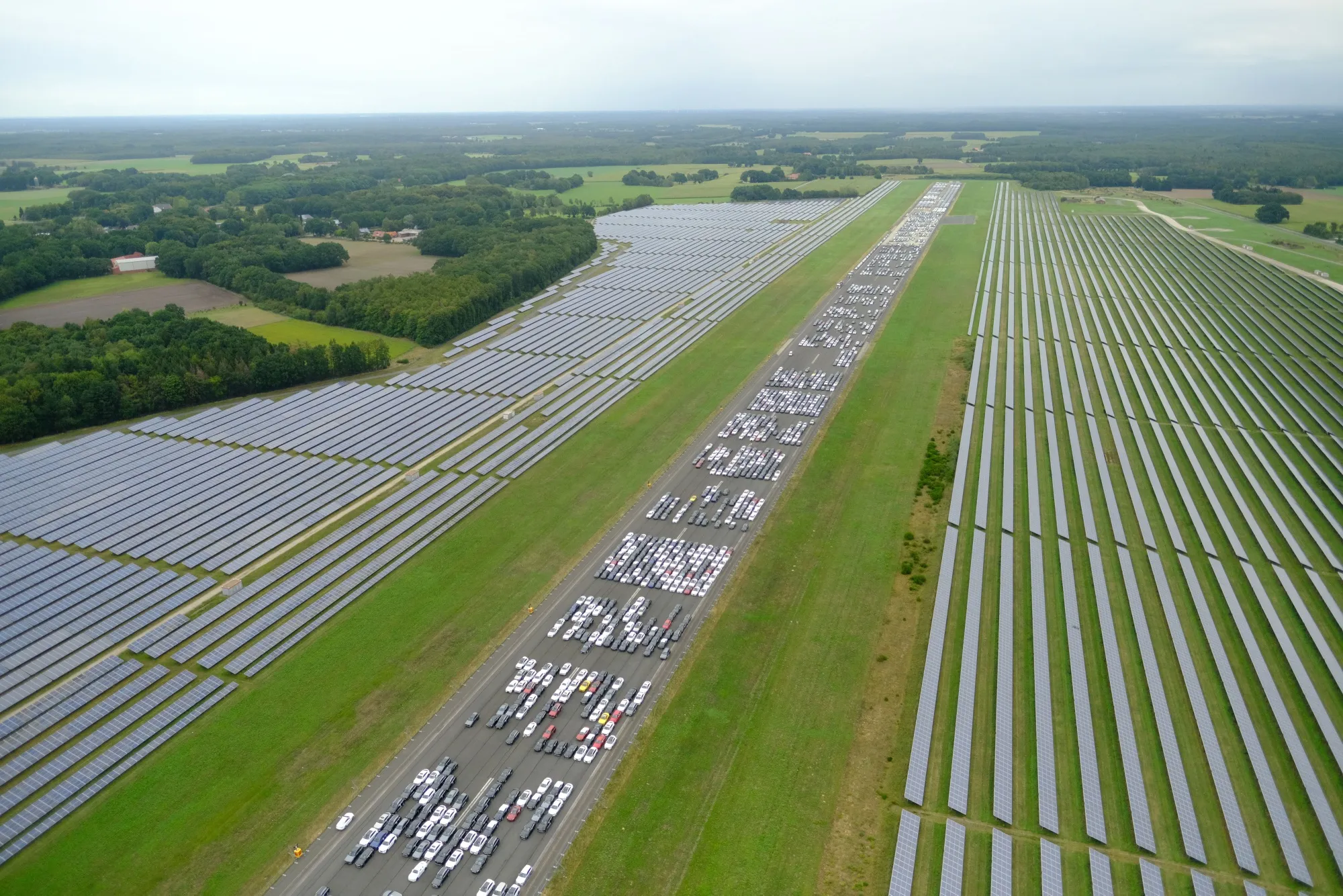 Automobiles stand on an airfield runway flanked by solar panels near Bremen, Germany
