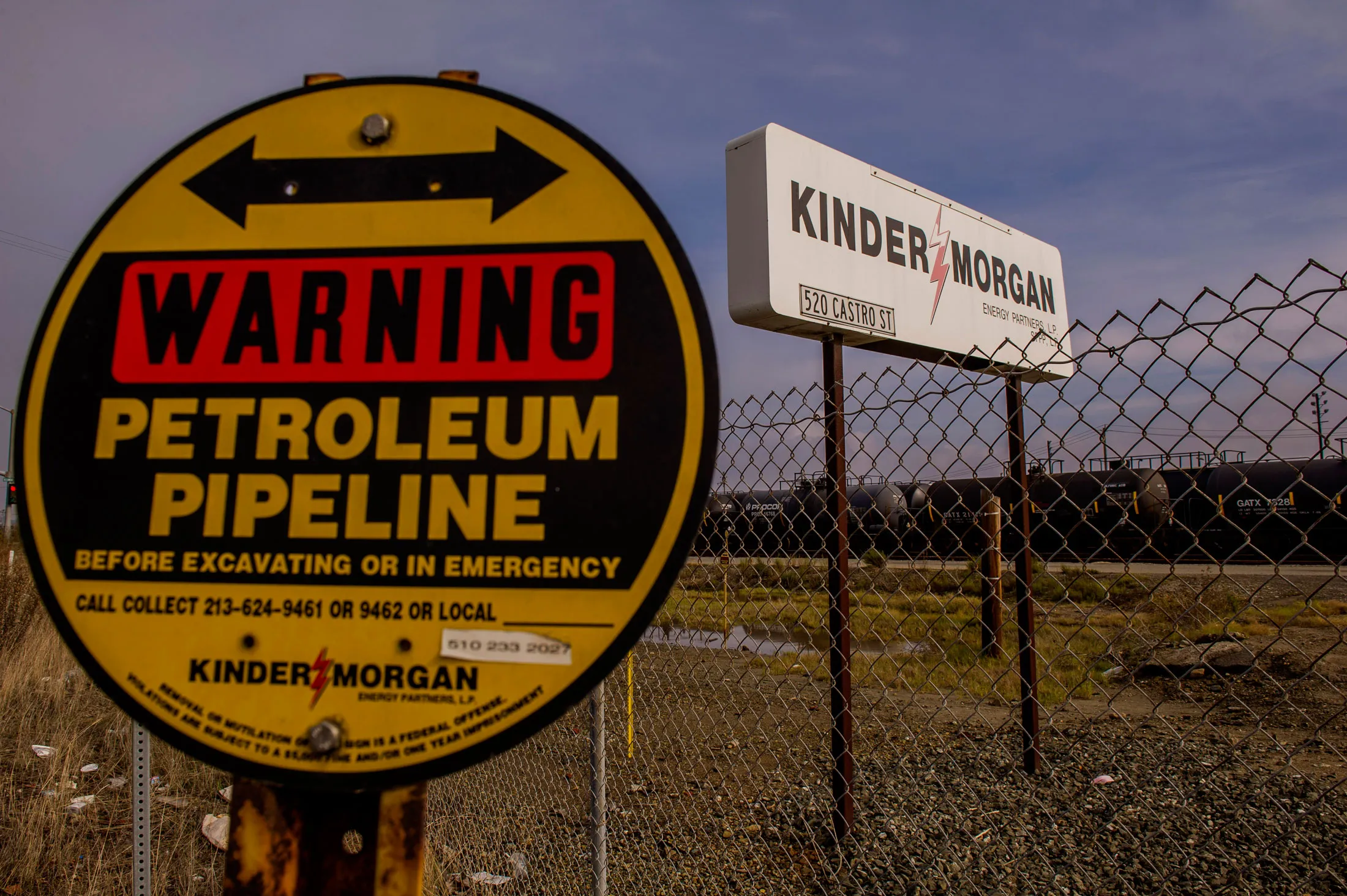 A warning sign for a petroleum pipeline stands in front of Kinder Morgan Inc. signage displayed at the company's facility in Richmond, California, U.S., on Friday, Nov. 21, 2014. Crude-oil handling facilities at the end of rail lines from Albany, New York, to Richmond, California, are mired in lawsuits filed by community and environmental groups claiming they were kept in the dark about the projects.
