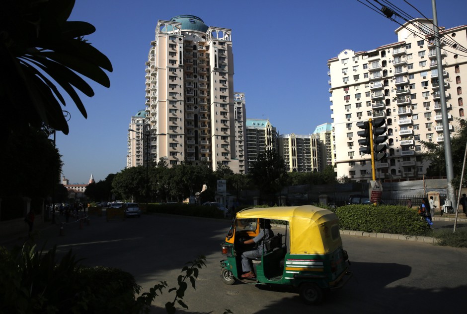 An auto rickshaw drives past a high-rise residential building complex in Gurgaon.
