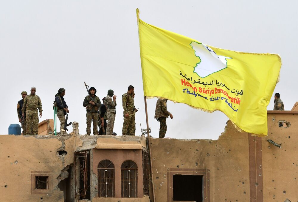 Les combattants des Forces démocratiques syriennes se tiennent au sommet d'un toit à côté de leur drapeau déployé à Baghouz, dans la province de Deir Ezzor, dans l'est de la Syrie.