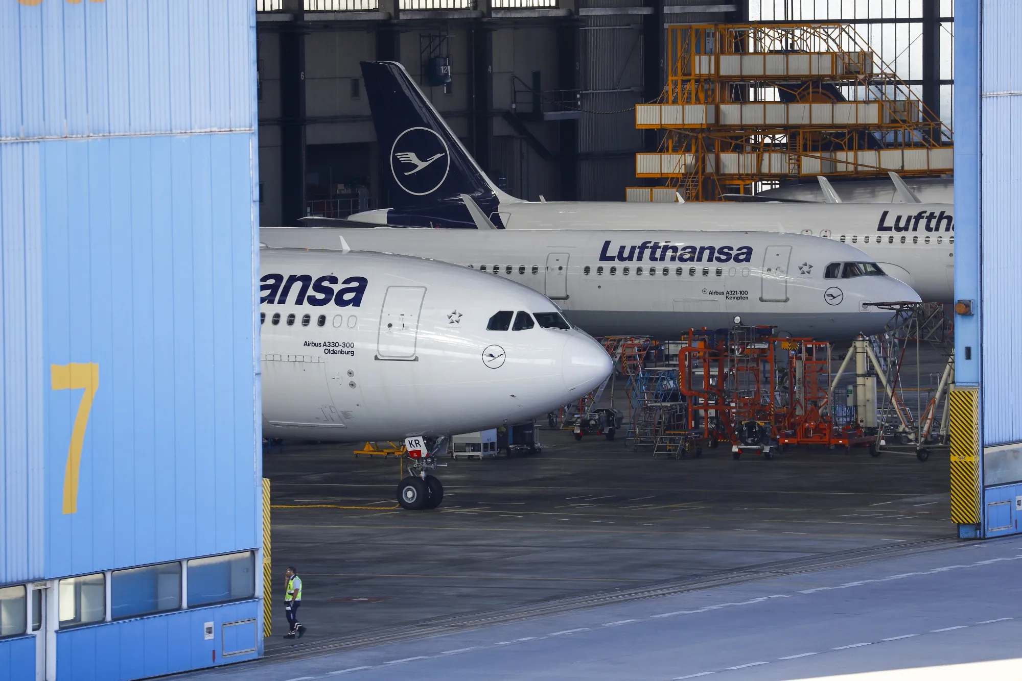 An employee passes Airbus SE A330-300, left, and A321-100 passenger aircraft, operated by Deutsche Lufthansa AG, in a hangar at Frankfurt Airport.