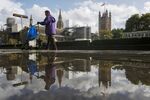 A municipal worker passes a reflection of the Houses of Parliament in a puddle in London, U.K.