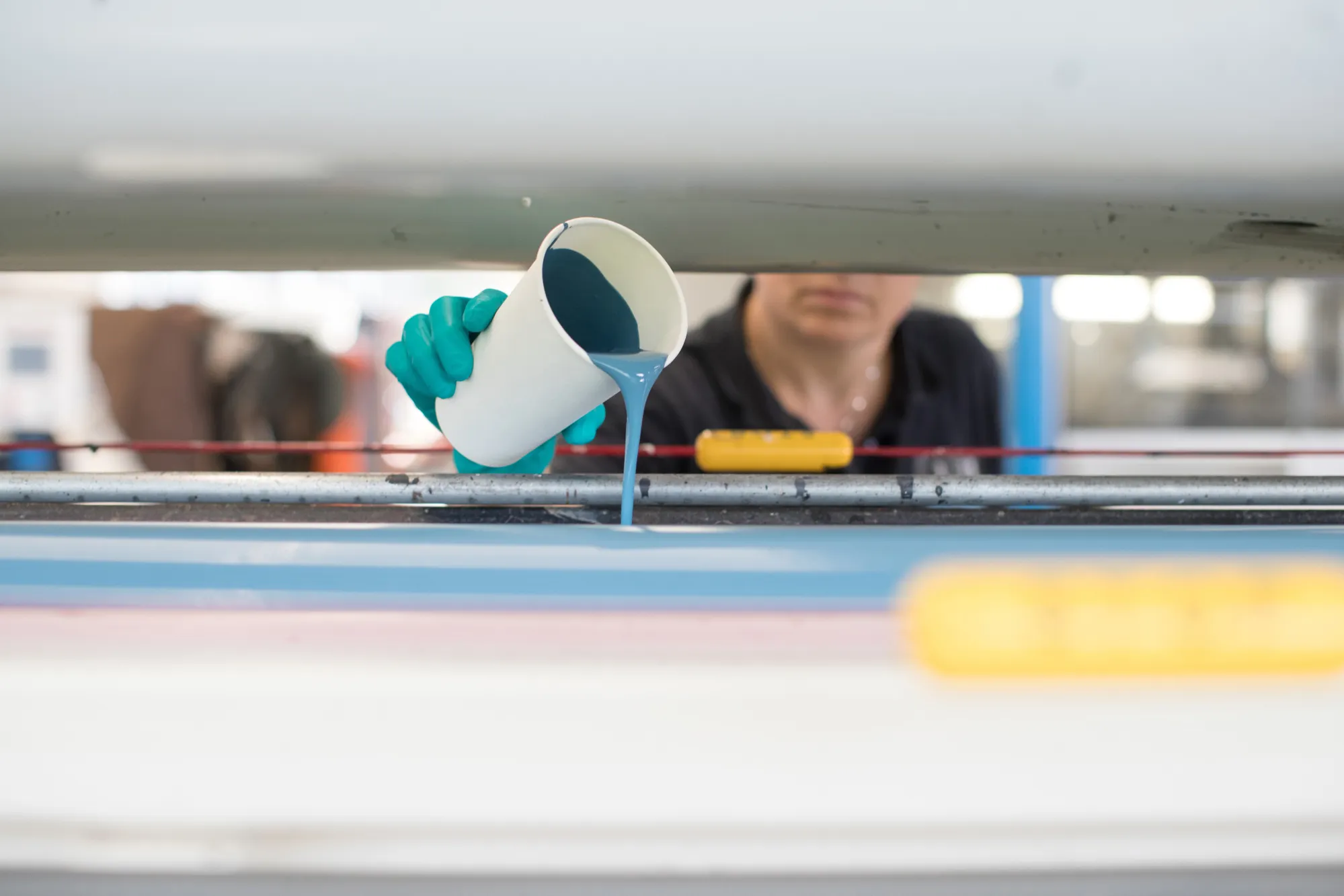 An employee pours a blue pigment base-coat on the rollers of an application machine inside laboratory at a Stahl Holdings factory in Waalwijk, Netherlands.