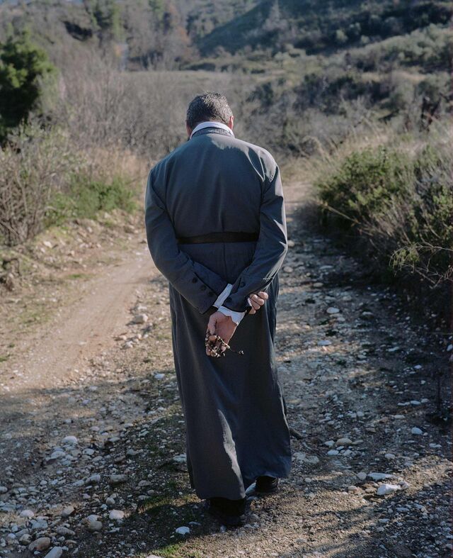 The back of Father Christos as he walks down a road in Evia Greece