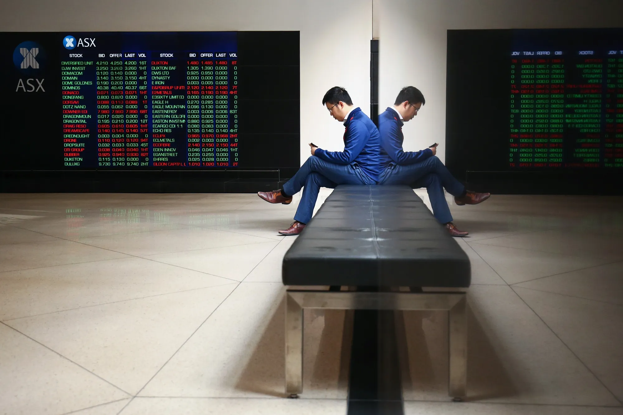 A man looks at his phone as an electronic board displays stock information at the Australian Securities Exchange, operated by ASX Ltd., in Sydney, Australia.