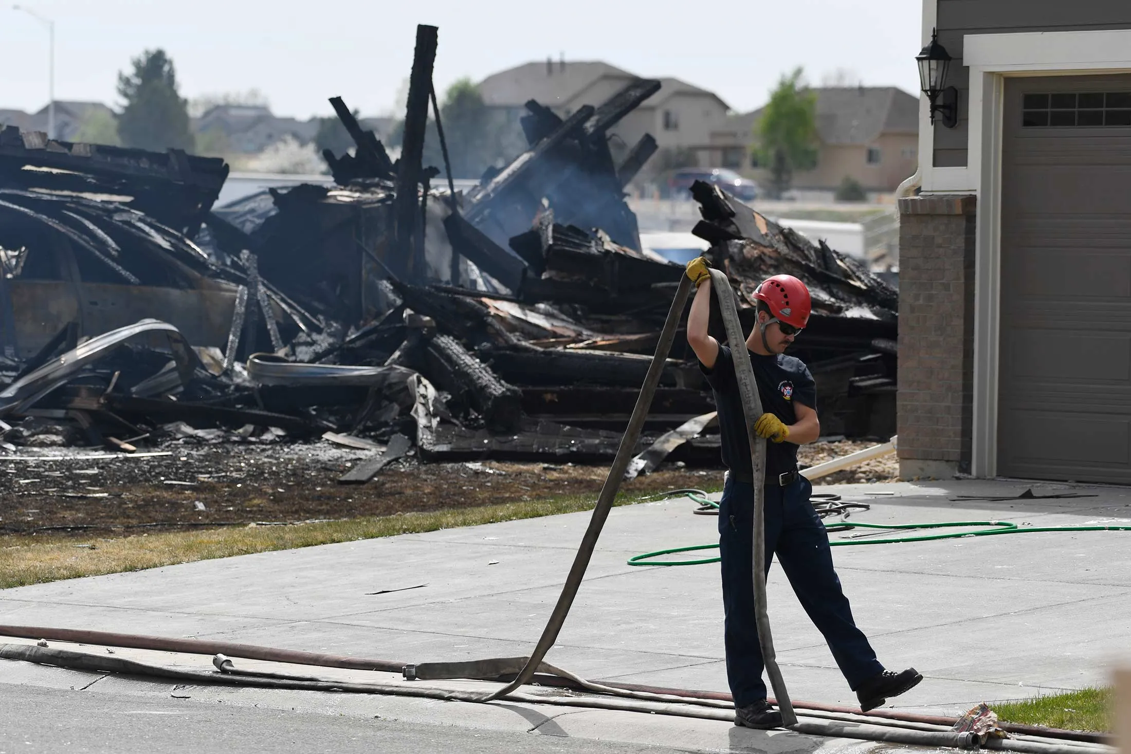 A Frederick-Firestone firefighter rolls up a hose in front of a burned out home April 18, 2017 in Firestone, Colo.
