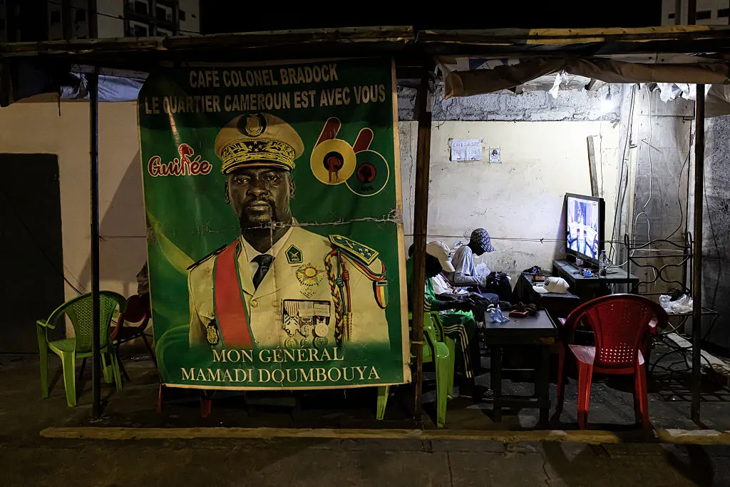 Residents watch television next to a poster depicting General Mamadi&nbsp;Doumbouya,&nbsp;in Conakry.