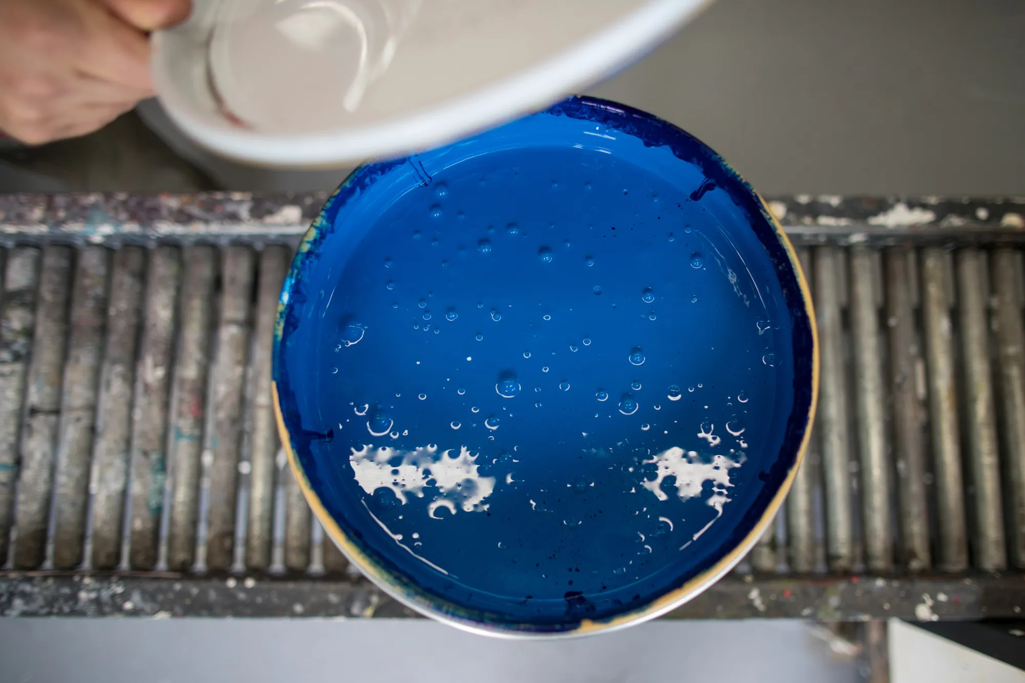 An employee places a lid on a tin of ready mixed blue paint inside the PPG Industries Inc. paints and coatings factory in Amsterdam, Netherlands.