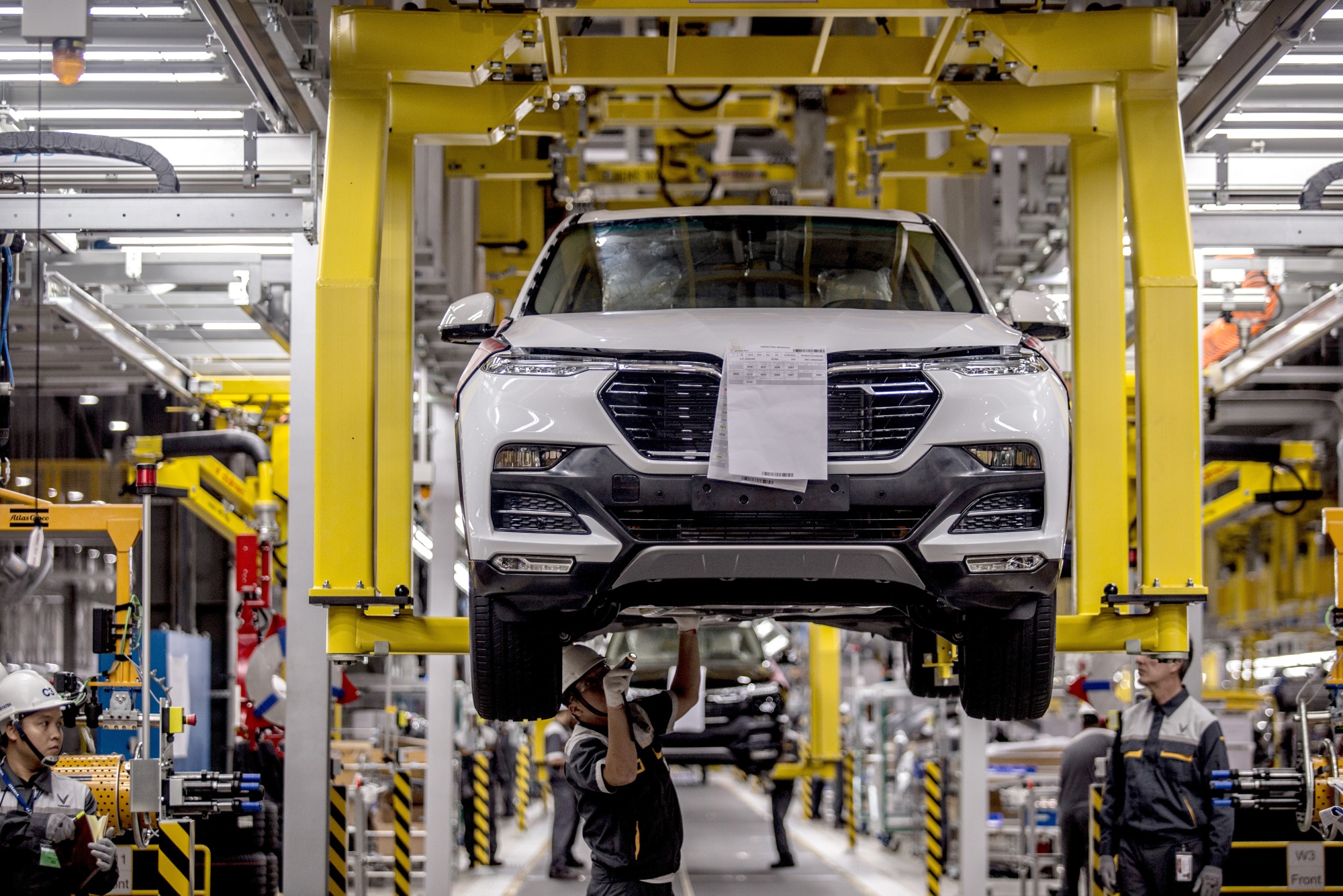 An employee looks under a VinFast&nbsp;SUV&nbsp;as it moves along an overhead conveyor on the assembly line on June 14.