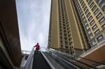 A pedestrian rides on an escalator past apartment buildings at China Evergrande Group's City Plaza development in Beijing, China, on Friday, Dec. 10, 2021.