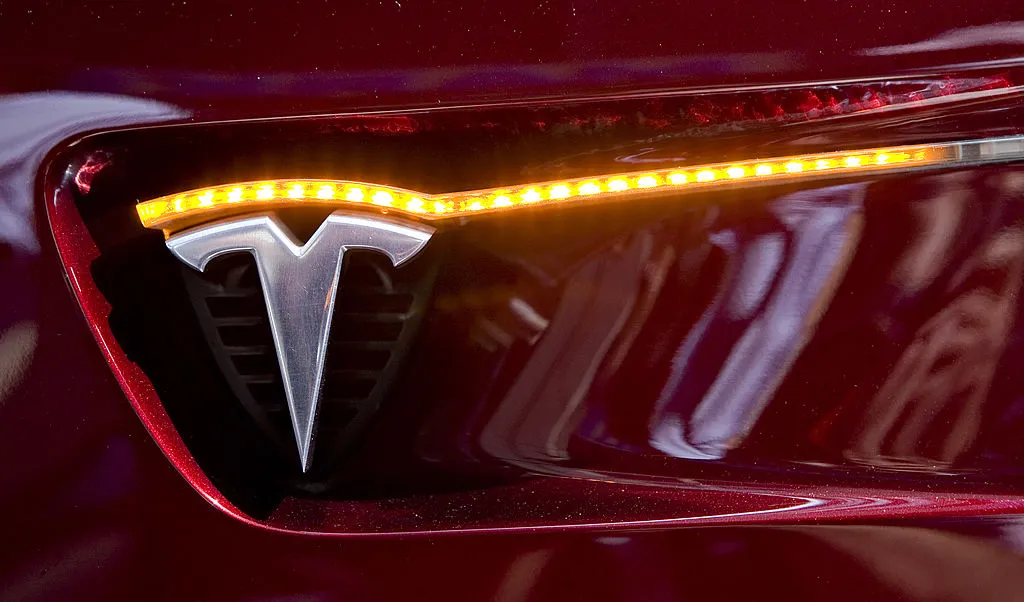 A Tesla logo appears on the side of a Tesla Model S electric sedan.