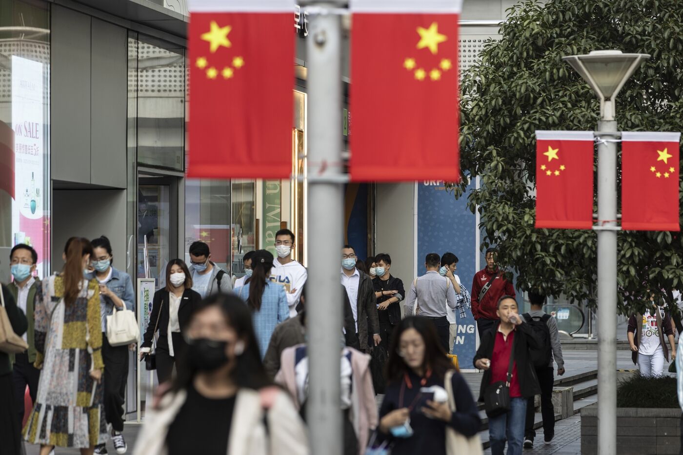 Morning commuters wearing protective masks walk past Chinese flags displayed along Nanjing Road in Shanghai, China, on Friday, 