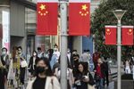 Morning commuters wearing protective masks walk past Chinese flags displayed along Nanjing Road in Shanghai, China, on Friday,