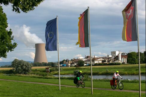 Cyclists ride beneath flags as Grohnde nuclear power plant stands beyond in July 2015.