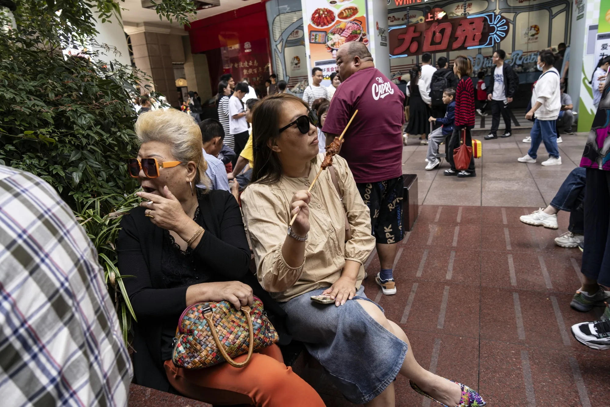 A woman enjoys a meat skewer while shoppers and visitors walk down one of the main retail streets in Shanghai this year.&nbsp;
