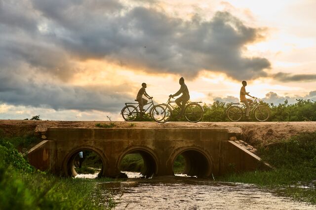 Th sun sets over cyclists riding across a bridge in in Nyimbamwana village.
