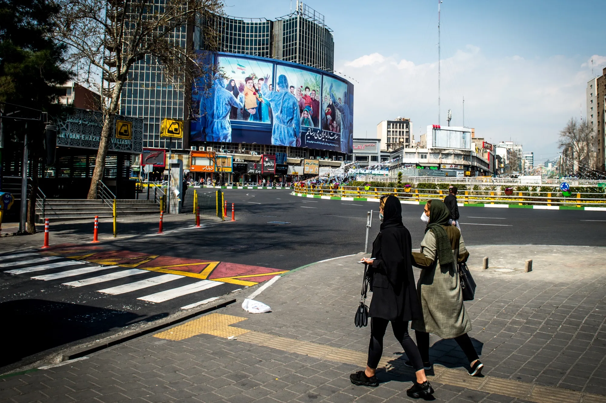 Pedestrians wearing protective face masks pass murals praising the medical services in central Tehran, on March 15.