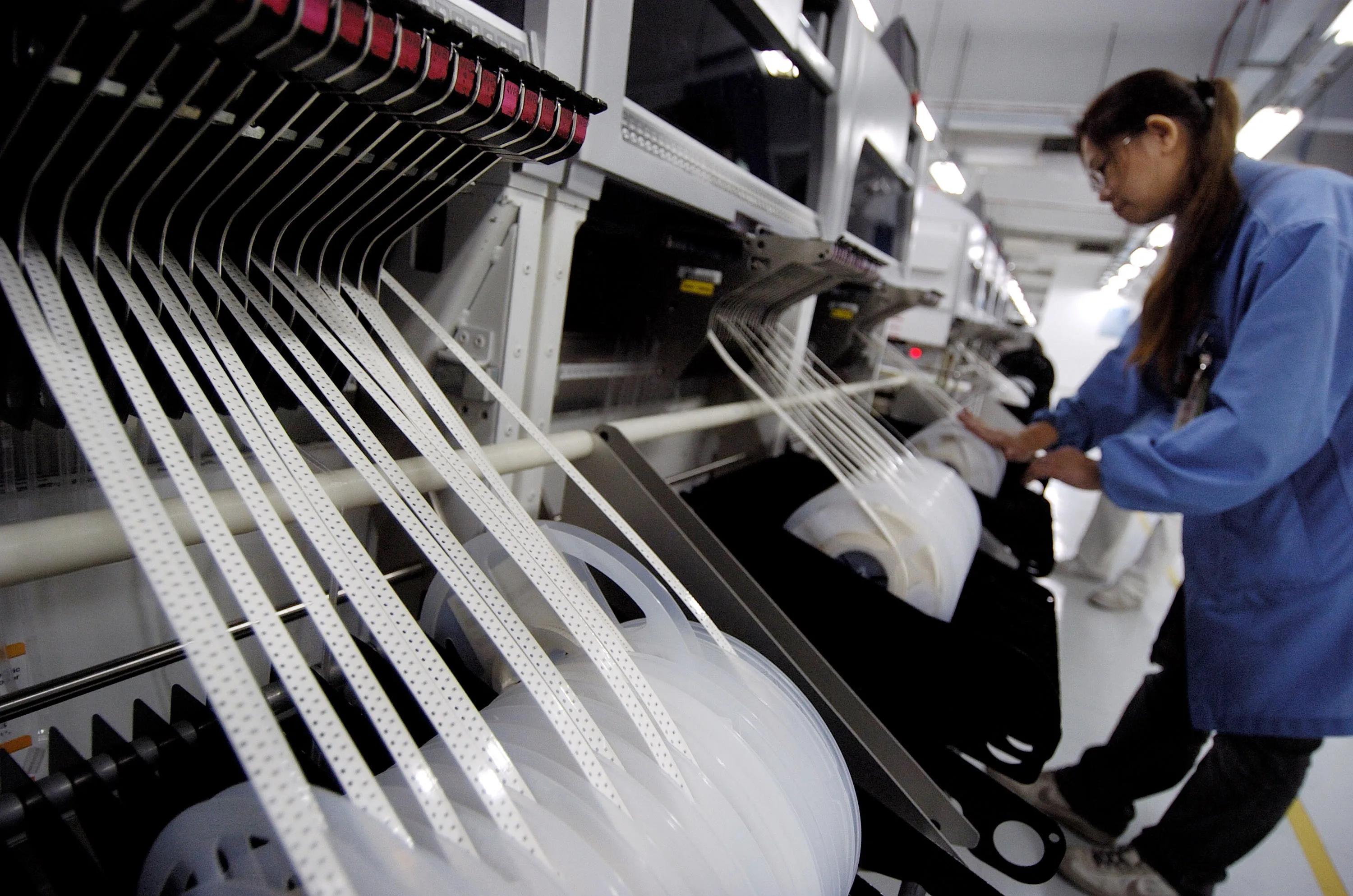 An Venture Corp. employee feeds chips into a surface mount machine on an assembly line at the company's factory in Singapore, Feb. 27, 2007.