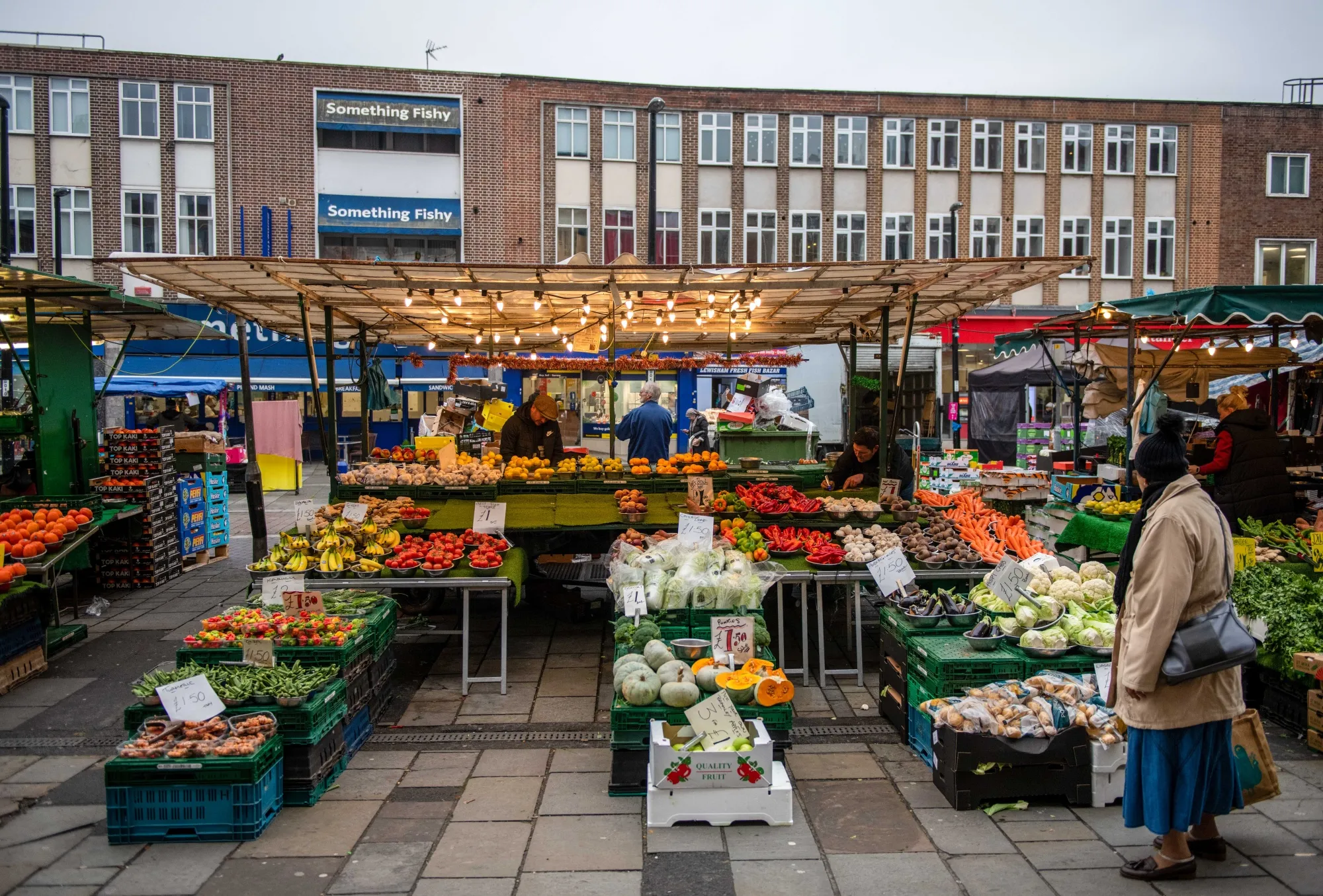 Shoppers browse and buy fruit and vegetables for sale at an independent greengrocer's market stall in London.