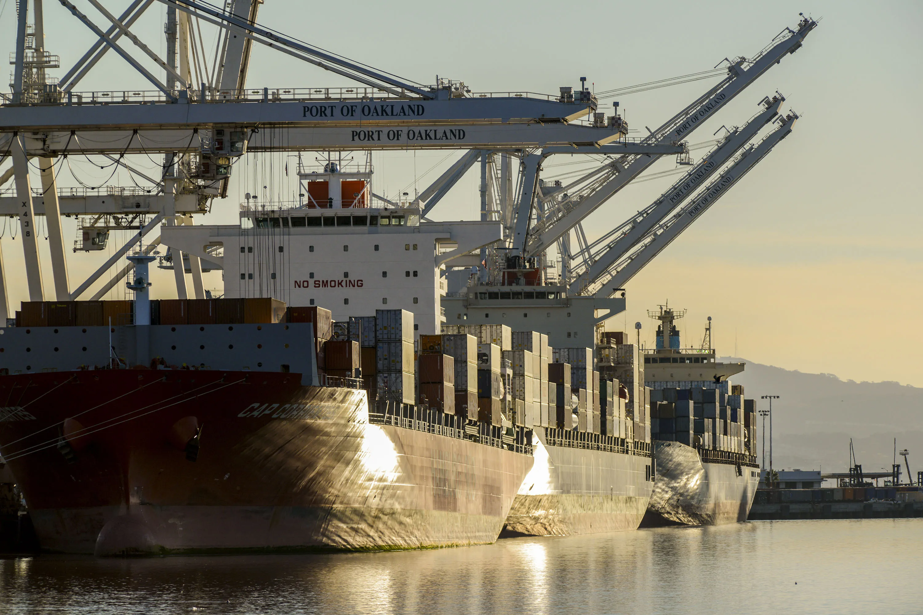 Container ships sit at a berth at the Port of Oakland in California.
