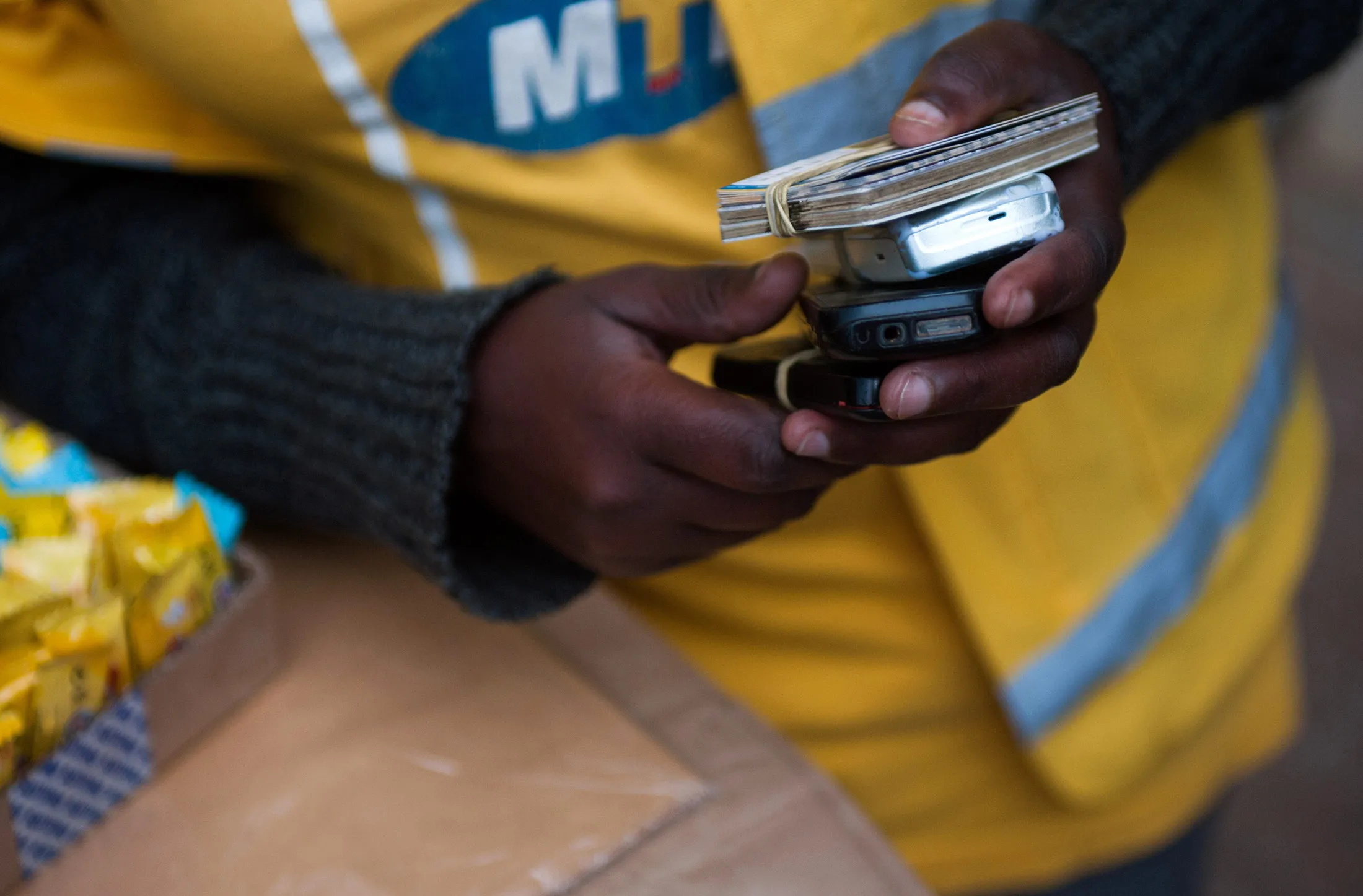 A vendor holds mobile phones and airtime scratch cards at a Mobile Money stall operated by MTN Group Ltd.
