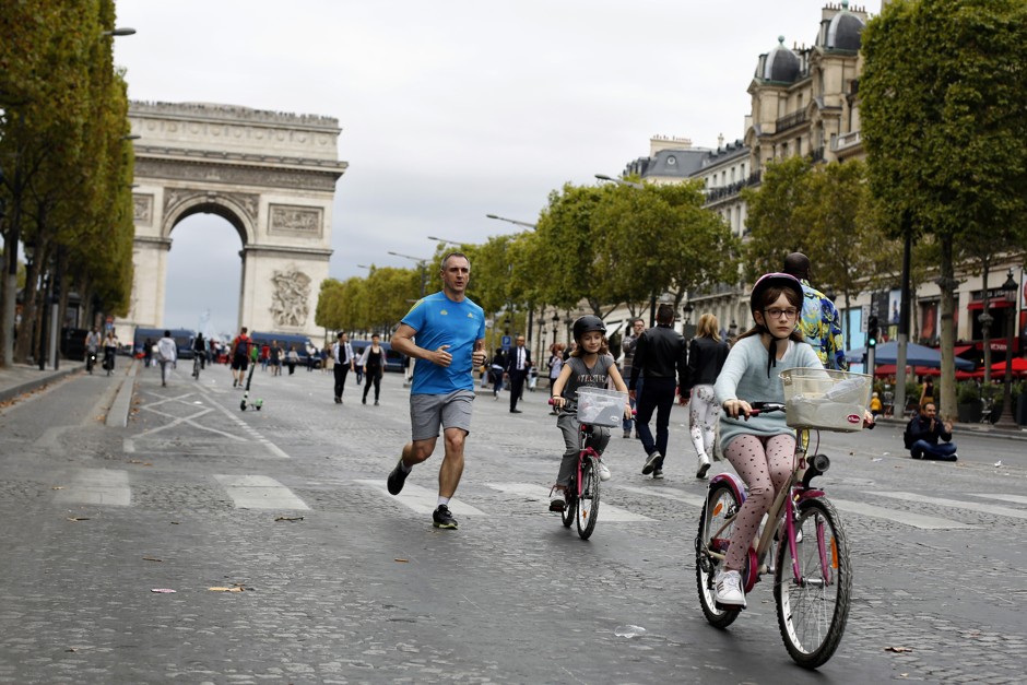 A man runs as his daughters bicycle on the Avenue des Champs-Élysées during a day without cars in Paris, Sunday, Sept. 22, 2019.