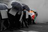 A crowd of protesters wearing helmets and masks hold umbrellas and makeshift wooden shields to block an oncoming cloud of tear gas