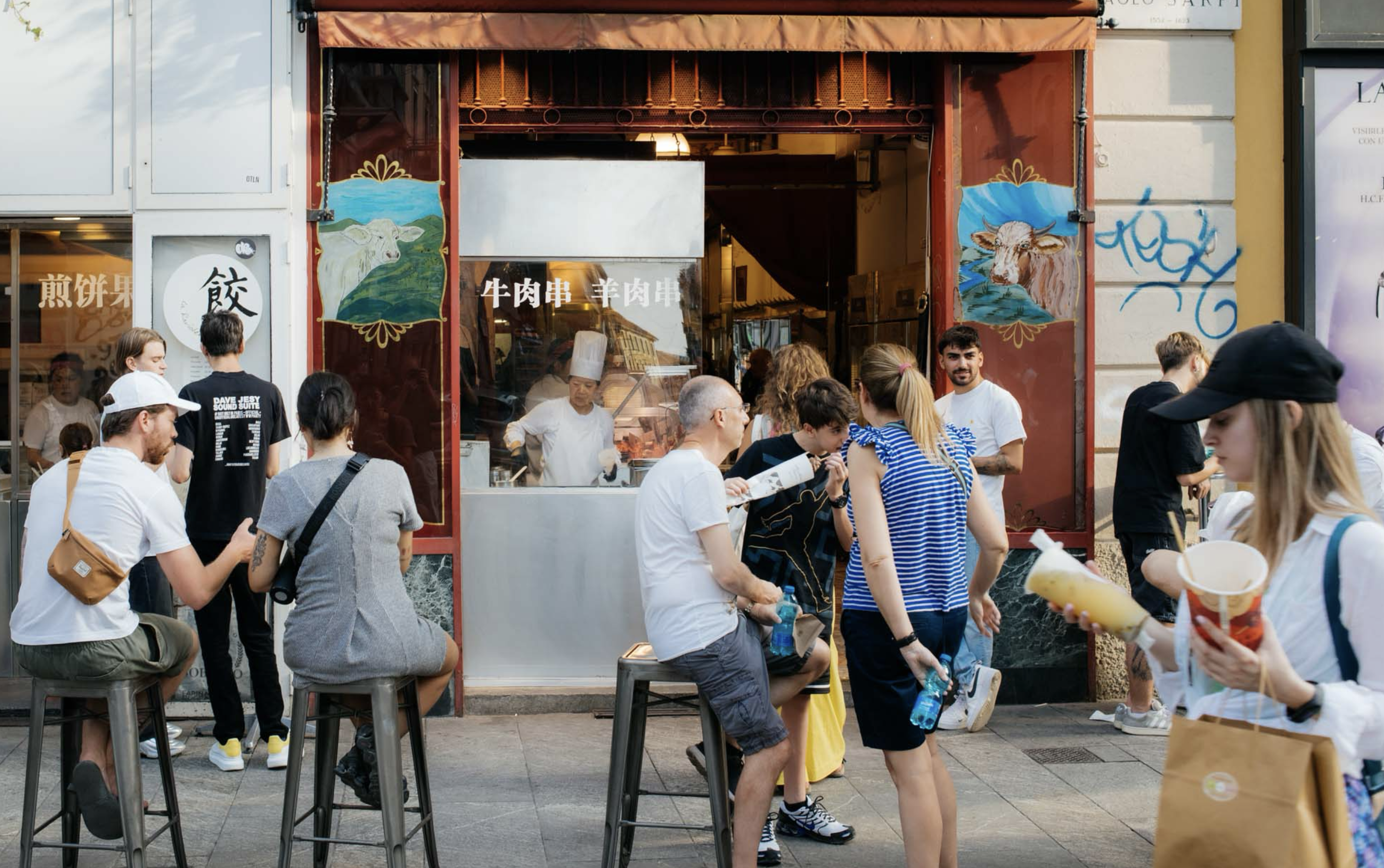 People wait on stools in front of a restaurant in Milan's Chinatown.