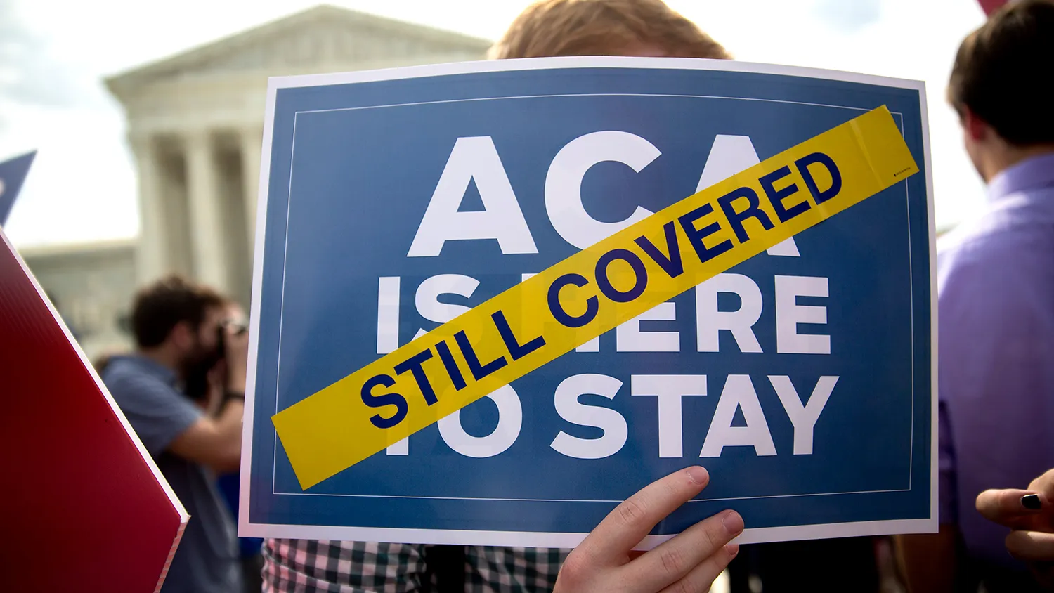 Demonstrator Ryan Thomas, a supporter of U.S. President Barack Obama's health-care law, the Affordable Care Act (ACA), holds an 'ACA is here to Stay' sign after the U.S. Supreme Court ruled 6-3 to save Obamacare tax subsidies outside the Supreme Court in Washington, D.C., U.S., on Thursday, June 25, 2015.

