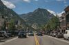 A main street in a rural town with cars circulating and forested mountains in the background