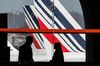 Passengers walk through the terminal as Tricolour livery sits on the tail fin of an Air France passenger aircraft beyond, operated by Air France-KLM Group, as it stands on the tarmac at Charles de Gaulle airport, operated by Aeroports de Paris, in Paris.