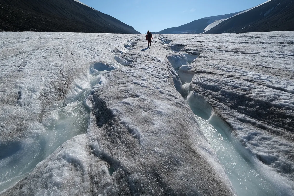 A hiker walks among winding channels carved by water on the surface of the melting Longyearbreen glacier near Longyearbyen, Norway.&nbsp;