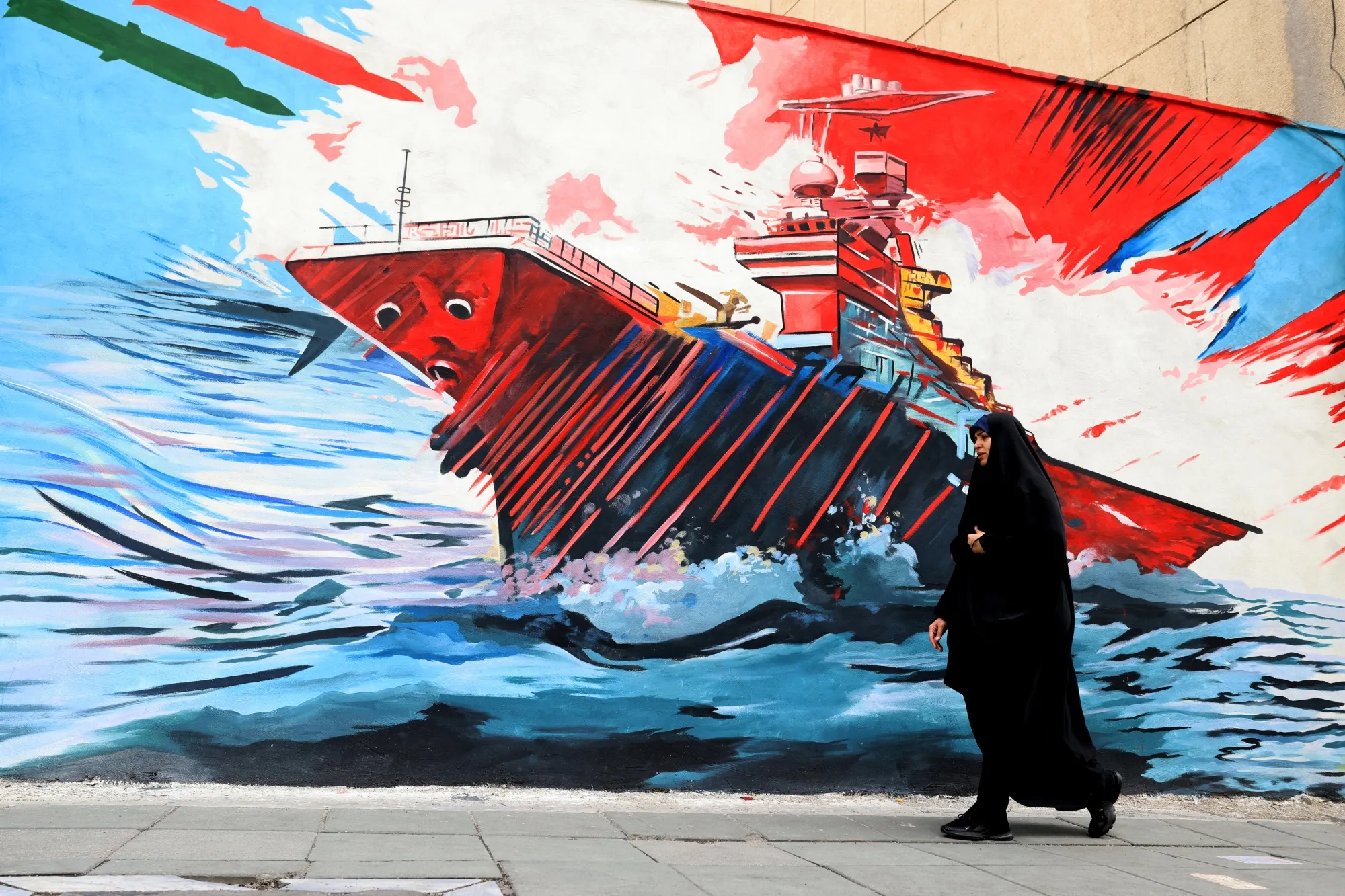 A woman walks past an anti-US and anti-Israel mural in Tehran.