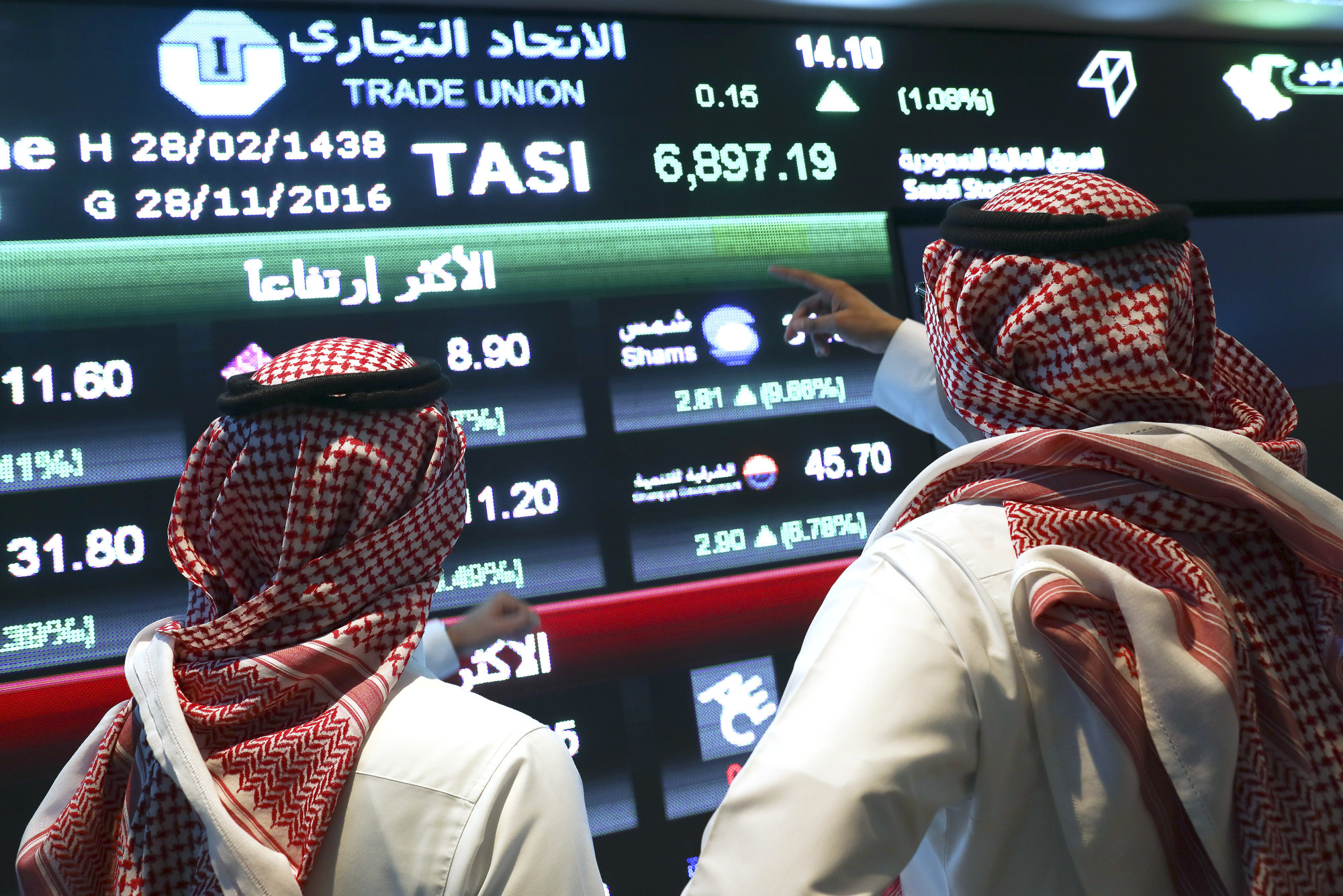 Visitors stand and watch stock movements displayed&nbsp;inside the Saudi Stock Exchange.