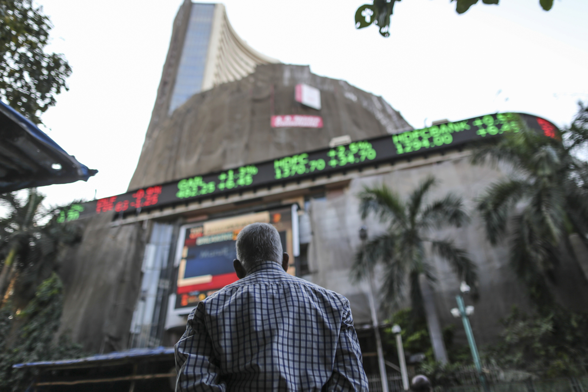 A man looks up at an electronic ticker board that indicates stock figures at the Bombay Stock Exchange in Mumbai, India.