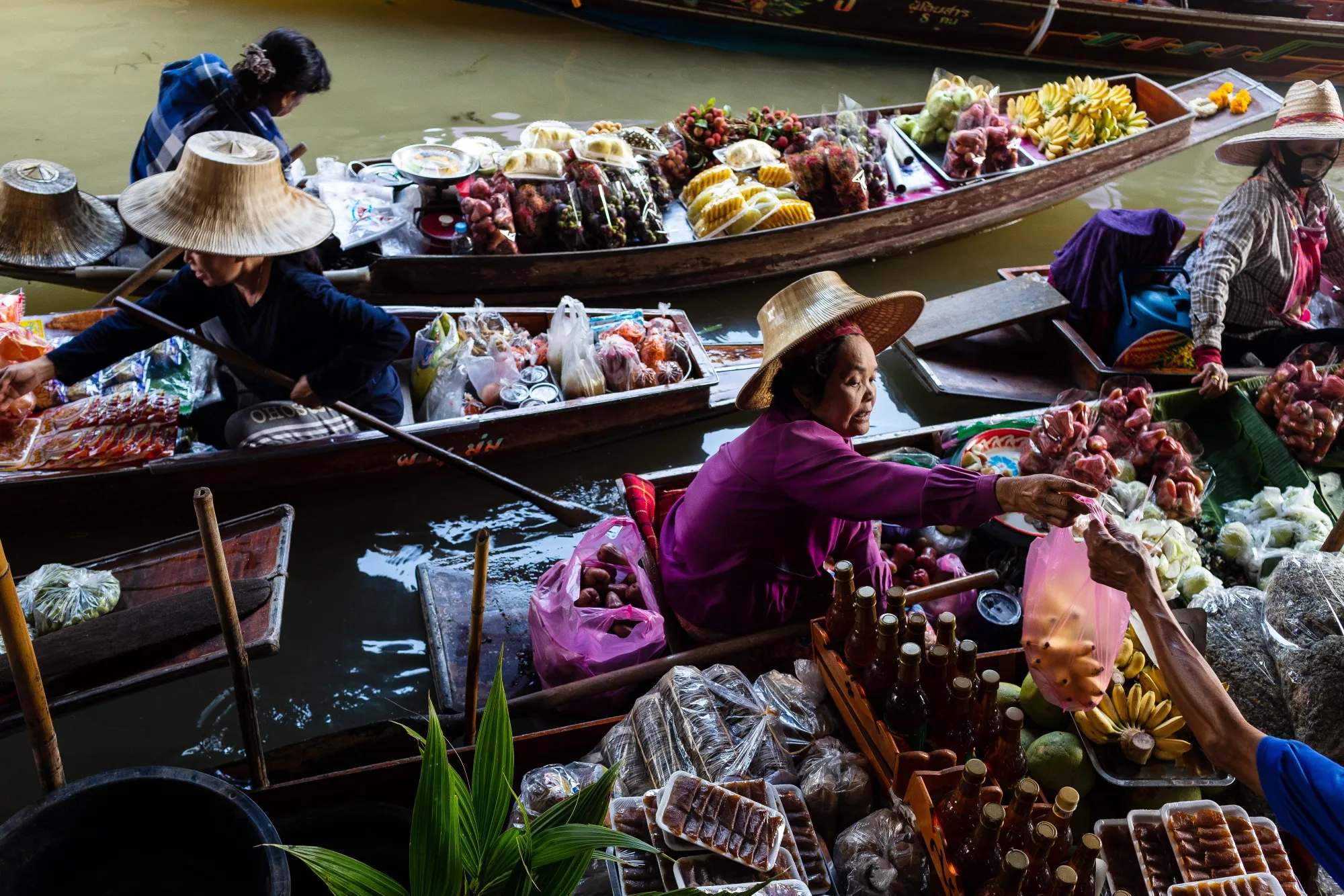 Vendors sort through fruits and goods while sitting on sampans in a canal at a floating market in Damnoen Saduak, Thailand.