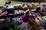 Vendors sort through fruits and goods while sitting on sampans in a canal at a floating market in Damnoen Saduak, Thailand.