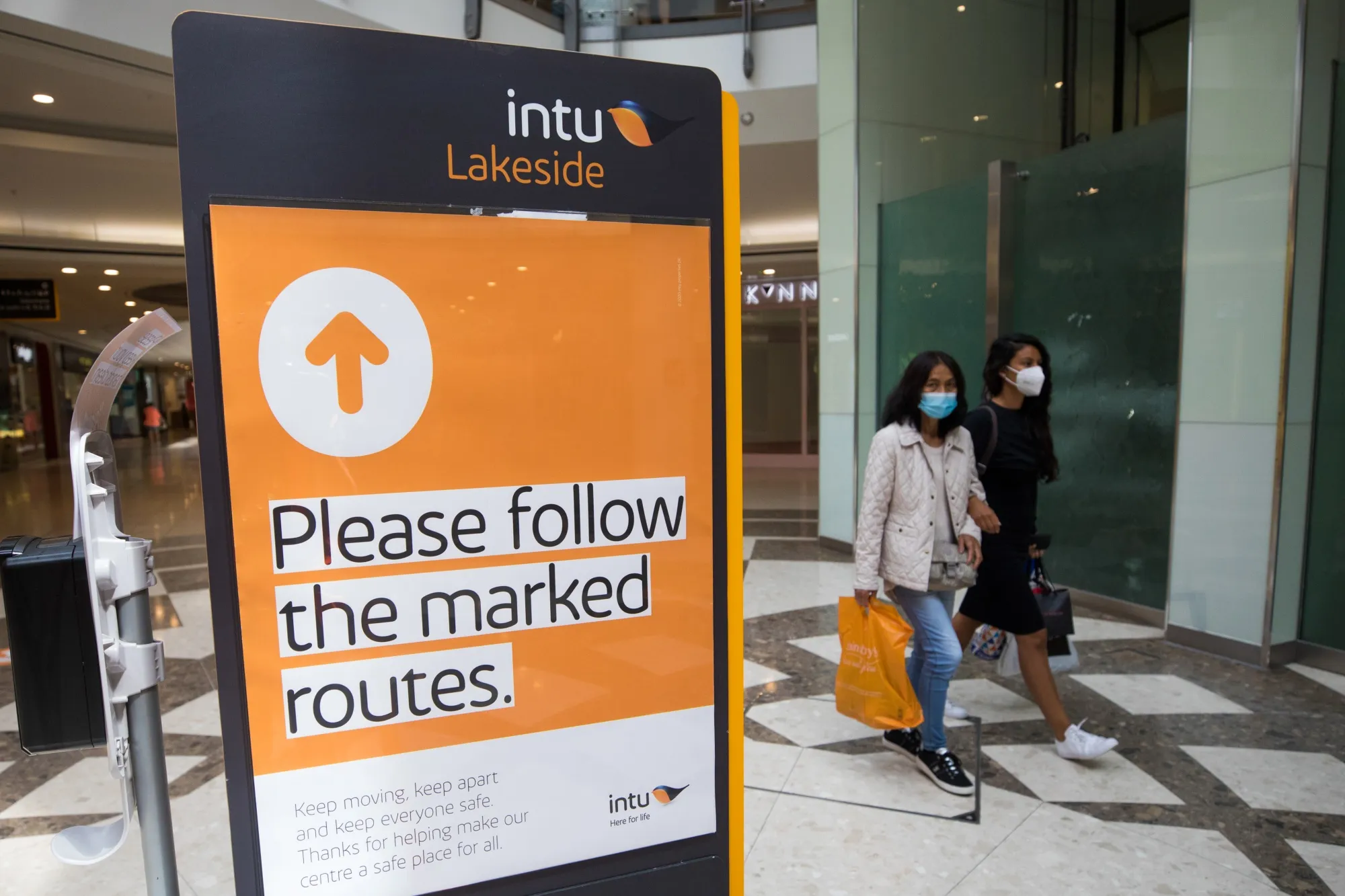 Shoppers pass a sign indicating the direction of walking around the Lakeside shopping centre, operated by Intu Properties Plc, in Thurrock, U.K.