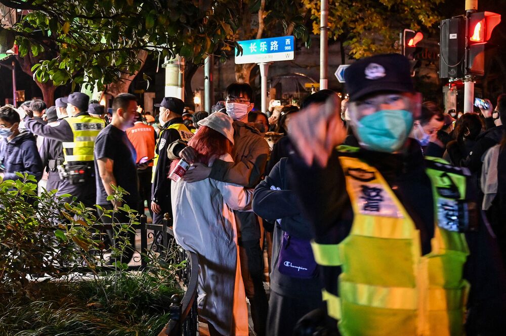 A man hugs a woman as police officers ask people to leave an area in Shanghai on November 27, 2022, where protests against China's zero-Covid policy took place the night before following a deadly fire in Urumqi, the capital of the Xinjiang region.