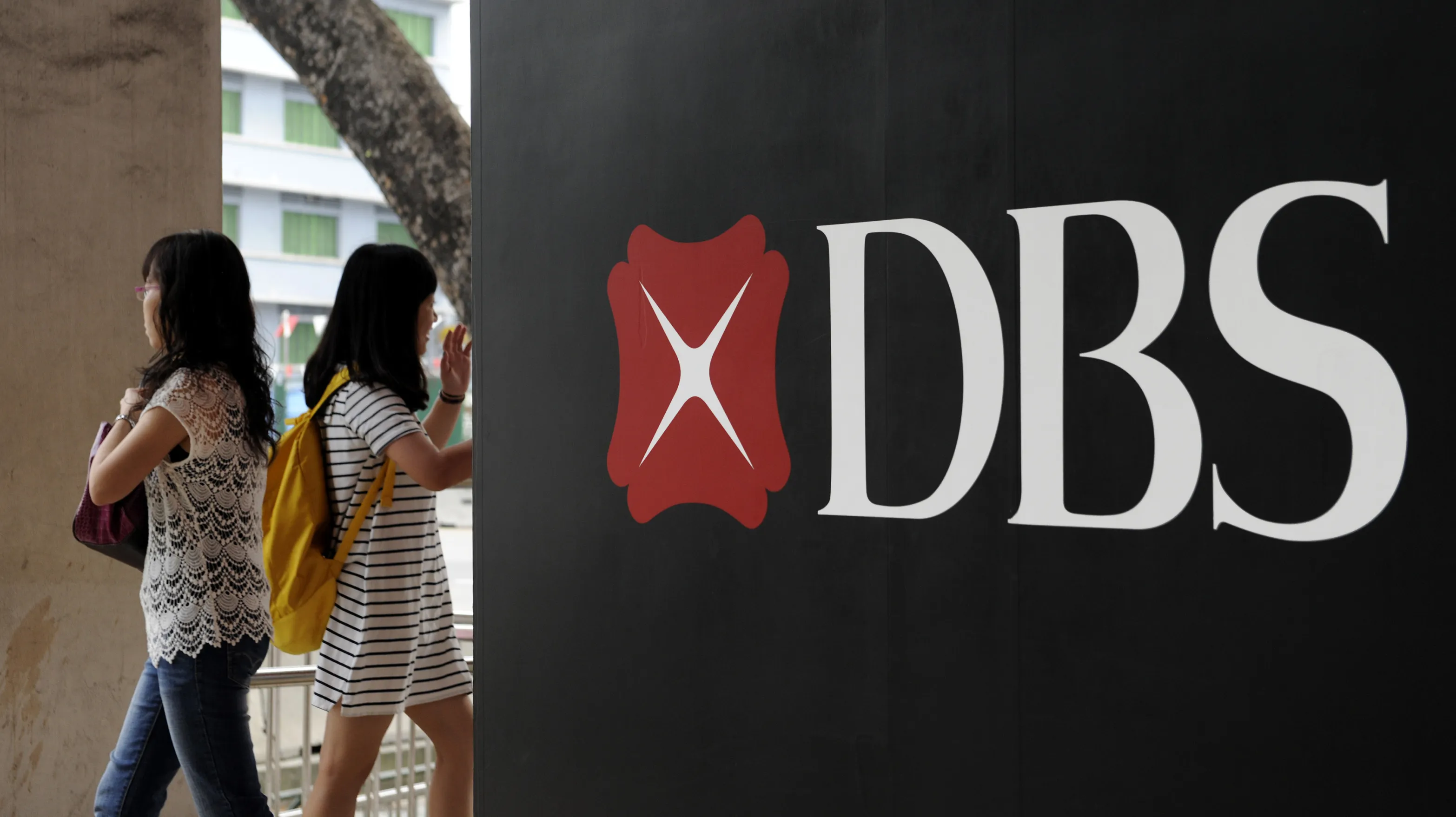 Pedestrians walk past the DBS Group Holdings Ltd. logo displayed outside a bank branch in Singapore.